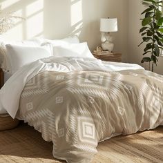 a bed with white comforters and pillows in a bedroom next to a potted plant