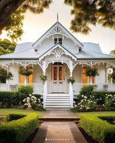 a white house that is next to some bushes and trees in front of the house