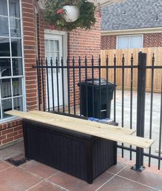 a wooden bench sitting in front of a black fence with a trash can next to it