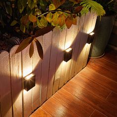 three lights are shining on the side of a wooden fence in front of a potted plant