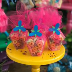 three plastic containers filled with cereal sitting on top of a yellow cake plate next to pink and blue decorations