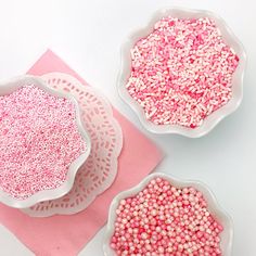 three bowls filled with pink sprinkles on top of a pink place mat