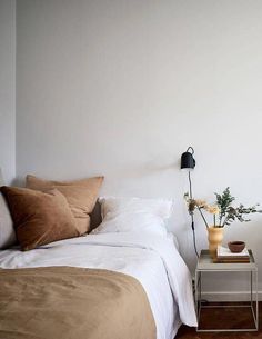 a bed with white sheets and brown pillows in a bedroom next to a lamp on the side table