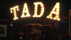 the word tada is lit up at night in front of a wall with pictures on it