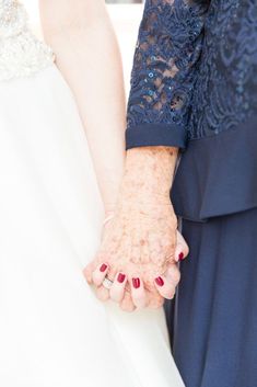 an older woman holding the hand of a younger woman in her wedding dress and wearing red nail polish