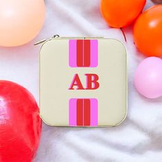 a pink and red case sitting on top of a white blanket next to some balloons