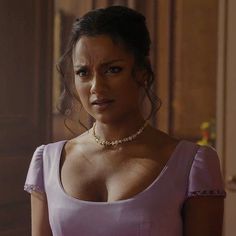 a woman in a pink dress is looking at the camera while wearing a pearl necklace