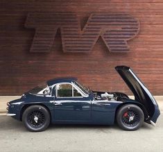 an old blue sports car with its hood open in front of a wooden sign that says bmw