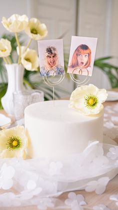 a white cake with two pictures on top and flowers in the middle, sitting on a table