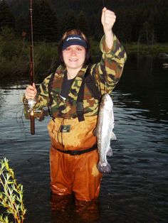 a man standing in the water holding a fish and a fishing rod with his right hand