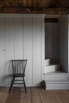 a black chair sitting in front of a white wall next to a stair case and wooden floor