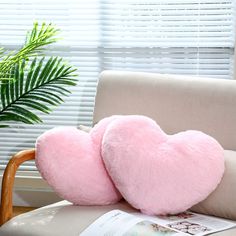 two pink heart shaped pillows sitting on top of a chair next to a plant and window