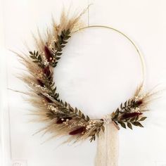 a wreath made out of dried grass and feathers on a white wall with a round frame