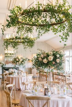 the tables are set with white flowers and greenery hanging from the ceiling above them