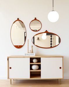 three mirrors are hanging on the wall above a cabinet