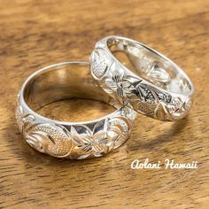 two silver wedding rings sitting on top of a wooden table next to each other,