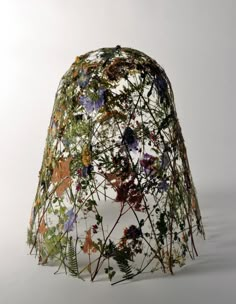 a hat made out of flowers and vines on a white background with the top partially covered by netting