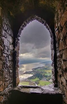 an open window in the side of a stone wall with water and land below it