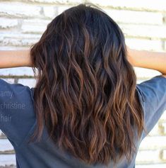 the back of a woman's head with long, wavy hair in front of a brick wall