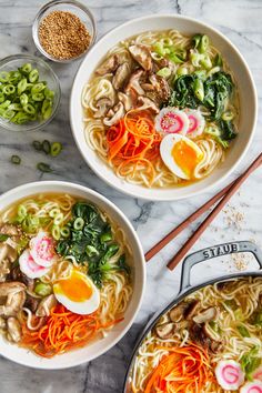 two bowls of ramen with eggs, carrots and broccoli on the side