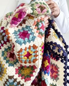 a woman is holding up a crocheted blanket