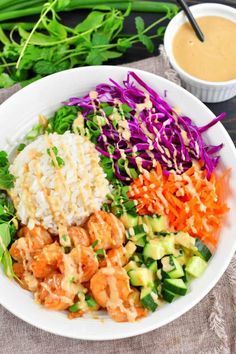 a white bowl filled with rice, carrots and veggies next to dipping sauce