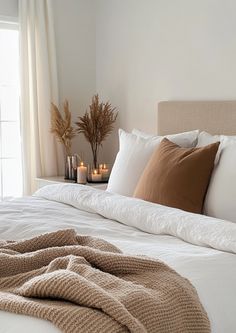 a white bed topped with pillows and blankets next to two candles on top of it