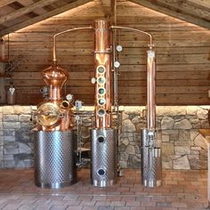 three large metal tanks sitting next to each other on a brick floor in front of a stone wall