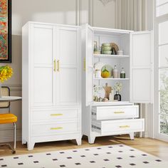 a white cabinet with yellow handles and drawers in a room next to a chair, table and window