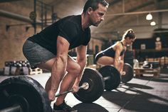 two men doing squats in a gym with barbells on the floor and one man lifting