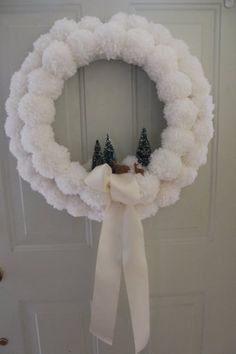 a white wreath hanging on the front door with two pine cones and trees in it