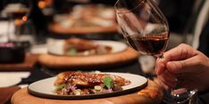 a person holding a wine glass over a plate with food on it