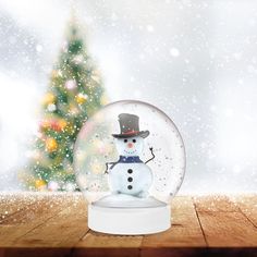 a snow globe with a snowman inside on a wooden table in front of a christmas tree