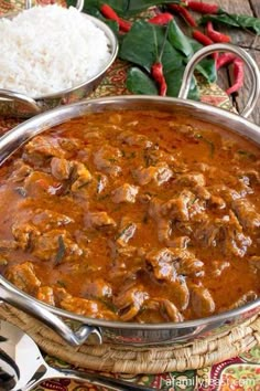 a large metal pan filled with food on top of a wooden table next to rice