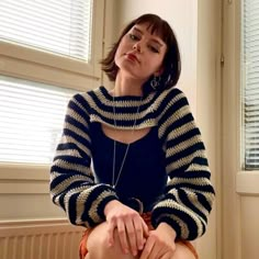 a woman sitting on top of a bed wearing a blue and white striped sweater over her body