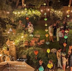 a group of people standing around each other in a yard with paper lanterns hanging from the ceiling