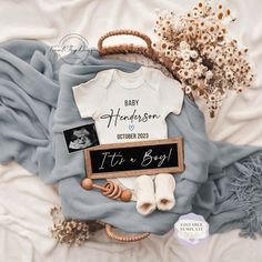 a baby announcement is displayed on top of a blanket with other items including a t - shirt, rattler, and flowers