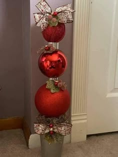 three red ornaments are stacked on top of each other in a metal vase with ribbons and bows