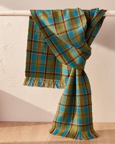 a green and blue plaid scarf hanging on a wooden floor next to a white wall