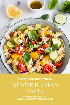 a bowl filled with pasta salad next to cucumbers and lemons on a table