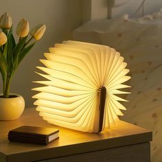 a lamp that looks like an open book sitting on a table next to a vase with tulips