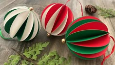 three christmas ornaments sitting on top of a wooden table next to green leaves and pine cones