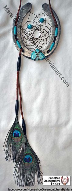 two peacock feathers are hanging from a metal object on a white sheet with blue beads