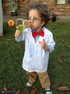 a little boy wearing glasses and a bow tie drinking out of a glass bottle while standing in the grass