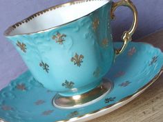 a blue cup and saucer with gold fleur de lis on the rim