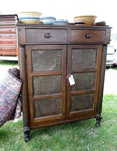 an old wooden cabinet sitting on top of a green grass covered field next to a pile of furniture