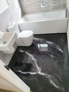 a white toilet sitting next to a bath tub in a bathroom on top of a black floor