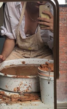 a woman sitting on top of two buckets filled with food and holding a cell phone