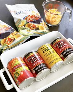 four cans of food sitting on top of a white tray next to bags of chips