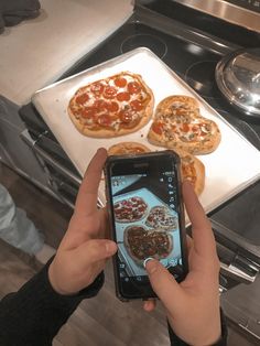 a person taking a photo of some pizzas on a stove top with their cell phone